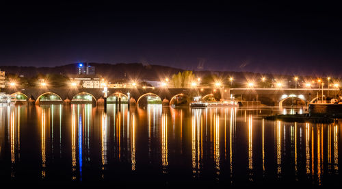 Illuminated bridge over river against sky at night