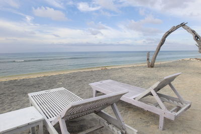 Empty chairs and table on beach against sky