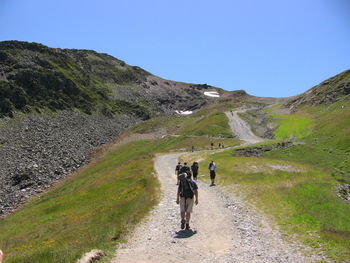 Rear view of people walking on mountain road against clear sky