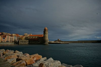 Buildings at waterfront against cloudy sky