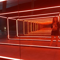 Rear view of woman walking on illuminated corridor at night