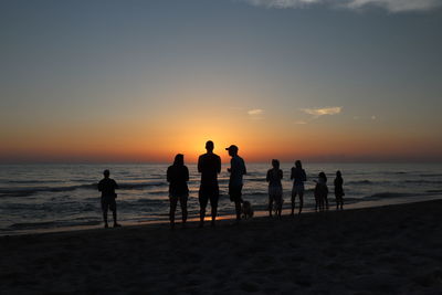 Silhouette people on beach against sky during sunset