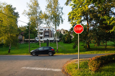 Stop sign with a black car in motion on a street behind in the daytime
