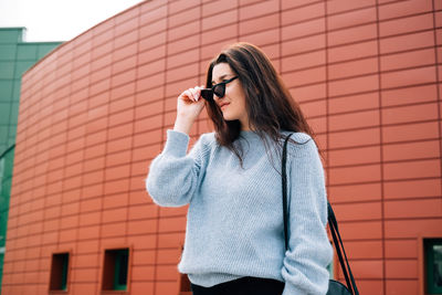 Young woman using mobile phone against brick wall