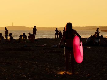 People on beach against clear sky during sunset