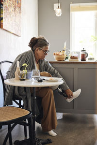 Woman with disability adjusting prosthetic leg while sitting on chair at home