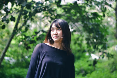 Portrait of young woman standing against trees