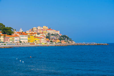 Scenic view of sea and buildings against clear blue sky