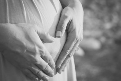 Midsection of pregnant woman making heart shape on belly