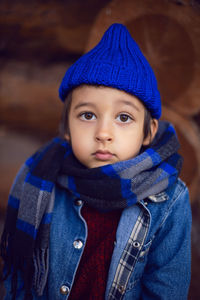 Boy child in a blue denim jacket and hat is sitting at a wooden house