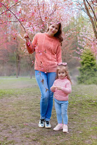 Happy mother and little daughter stand in park under pink cherry blossom .