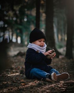 Baby boy holding pine cones while sitting on field in forest
