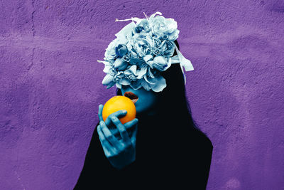 Close-up of hand holding purple rose against wall