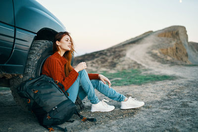 Young woman sitting on mountain against sky