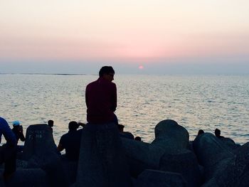 Rear view of couple on beach against sky during sunset