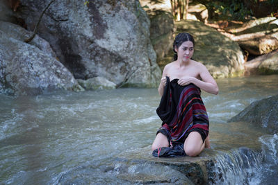 Young woman kneeling on rock in river