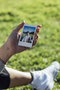 Woman holding instant transfer photograph while sitting on grass