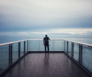 Rear view of man walking on pier over sea against sky during sunset