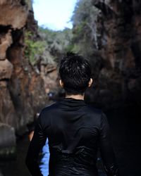 Rear view of teenage boy standing by rock formations