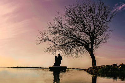 Silhouette woman standing by lake against sky during sunset