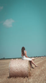 Side view of woman sitting on field against sky