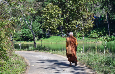Rear view of monk walking on road by lake