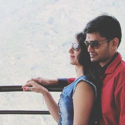 Side view of couple wearing sunglasses standing by railing