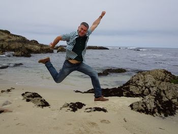 Full length of man jumping on rock at beach against sky