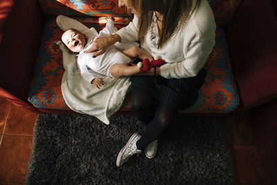 From above of satisfied mom touching baby playing with excited newborn infant with open mouth having fun lying on bed at home