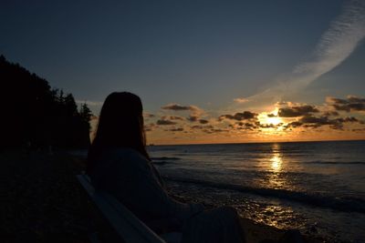 Woman sitting on beach against sky during sunset