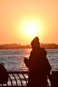 Silhouette man sitting on beach against orange sky