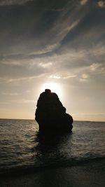 Silhouette rock formation in sea against sky during sunset