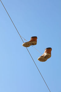 Low angle view of man hanging on rope against clear blue sky