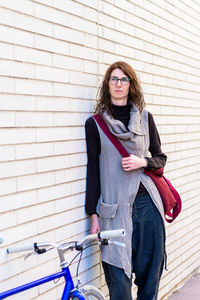 Young woman leaning on a city wall with vintage bike in sunny day