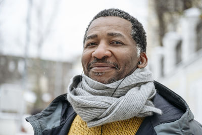 Smiling mature man wearing warm clothing listening to music through in-ear headphones