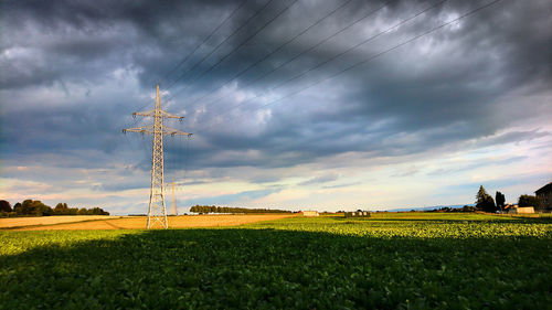 Electricity pylon on field against storm clouds