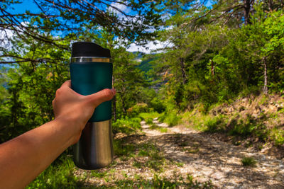 Cropped image of man holding bottle against trees in forest