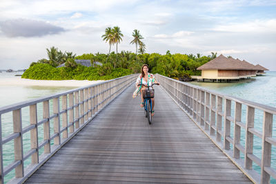 Rear view of woman walking on footbridge against sky