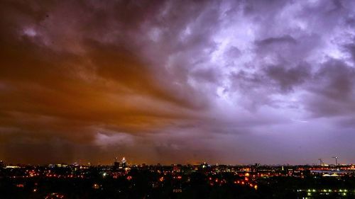 Illuminated cityscape against cloudy sky