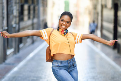 Portrait of cheerful young woman with arms outstretched standing on street