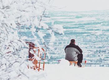 Rear view of man sitting on a slide against snow covered cityscape  