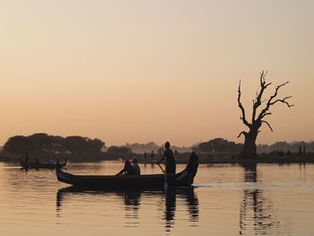 Silhouette people in boat against sky during sunset