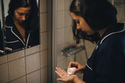 Woman taking pills while standing in front of mirror at bathroom