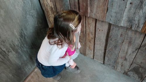 High angle view of girl peeking through wood paneling while hiding in cabin