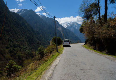 Road amidst trees and mountains against sky