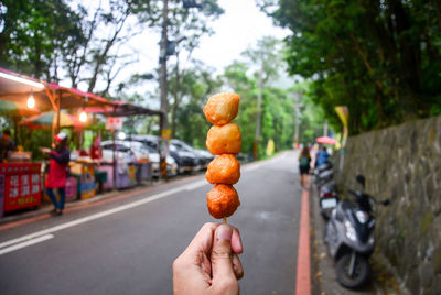 Street food, hand holding deep fried shrimp ball on the wooden skewer with food stall background