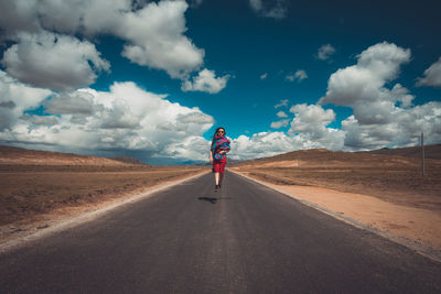 Woman jumping while running on road against sky