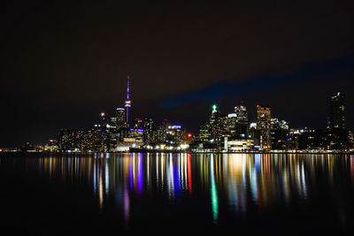 Illuminated buildings by river against sky at night