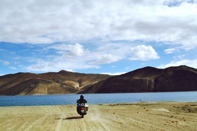 Rear view of man riding motorcycle on against lake against sky