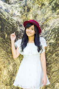 Portrait of smiling young woman wearing hat standing against rock formation